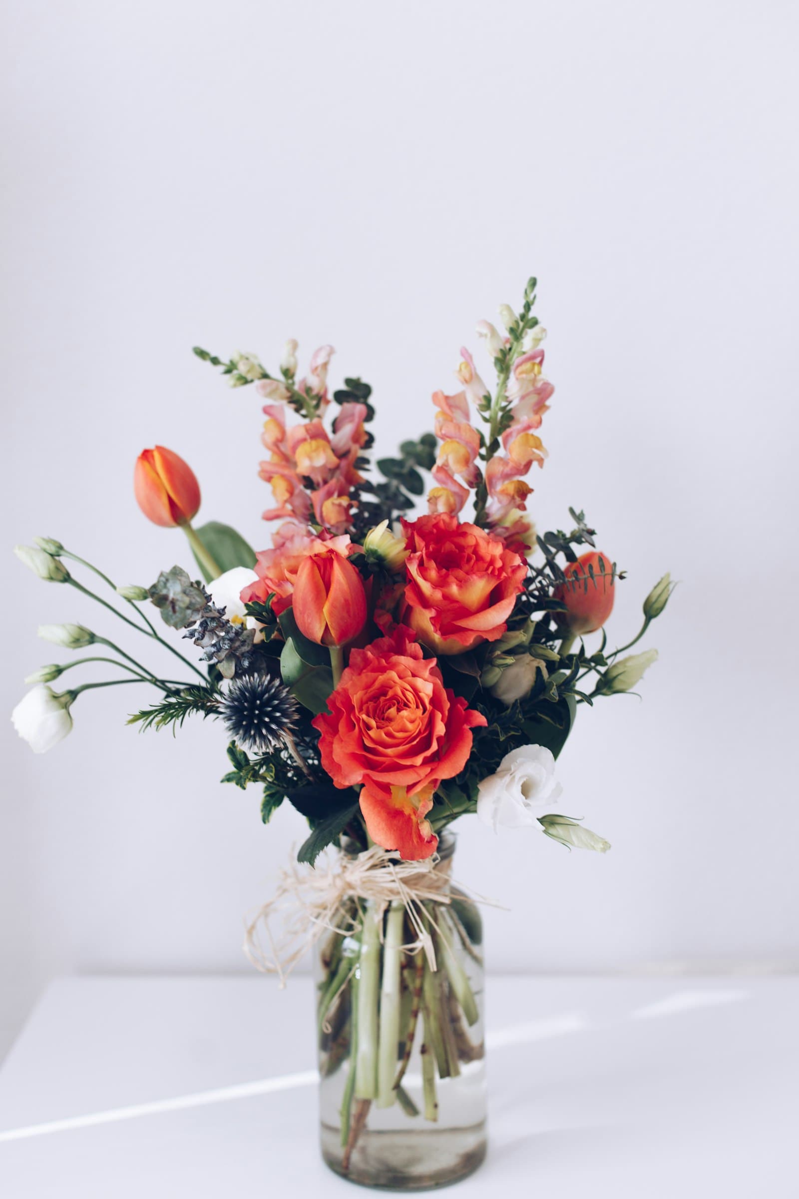 Orange roses, snapdragons and thistle in a glass vase